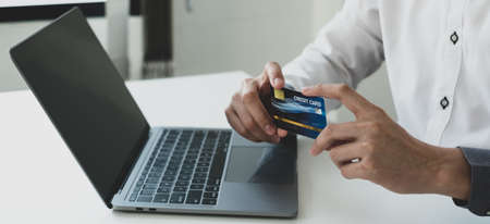 The businessman's hand is holding a credit card and using a laptop for online shopping and internet...