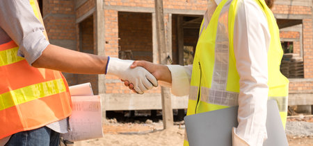 Shake hand, the team of male and female engineers or architects is exploring and inspecting the outdoor construction site work.の写真素材