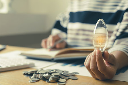 Hand of a businesswoman's hand Innovative and inspired by light bulbs and coins, Calculating financial graphs to build a successful business. Concepts of energy and money accounting.の写真素材