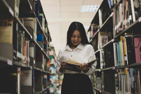 Young Asian women are searching for books and reading books on the tables and aisles of the college libraries to research and develop their academic and education self.の写真素材