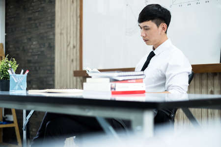 An Asian male teacher at the university is preparing lessons to teach in the classroom.の写真素材