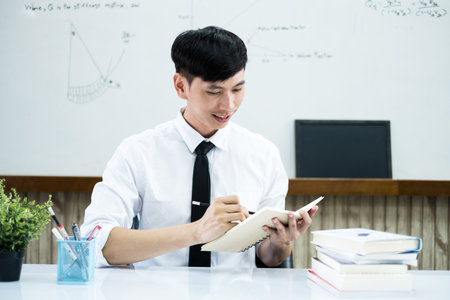 An Asian male teacher at the university is preparing lessons to teach in the classroom.の写真素材