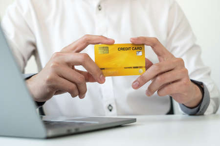 The businessman's hand is holding a credit card and using a laptop for online shopping and internet...