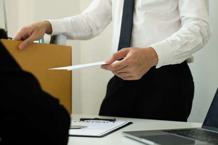 Desperately fired man office worker employee hands her employer her resignation letter and packs her belongings in a cardboard box concept dismissal and unemployment.の写真素材