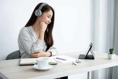 Video Calling a young Asian woman wearing headphones communicates via online long-distance video on...