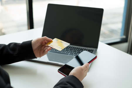 The businesswomen's hand is holding a credit card and using a laptop for online shopping and...