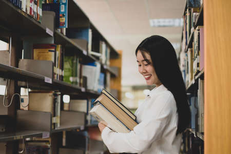 Young Asian women are searching for books and reading books on the tables and aisles of the college libraries to research and develop their academic and education self.の写真素材