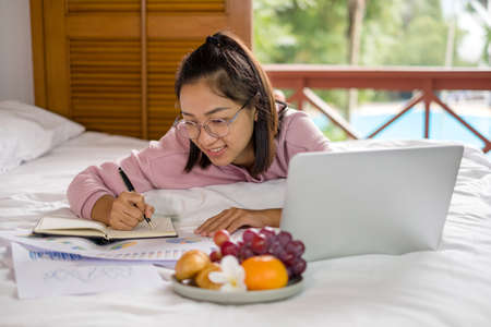 work from home, a young Asian woman who works in finance at home calculates financial graphs showing the results of his investments, planning the steps of his business growth.の写真素材