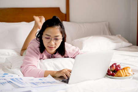work from home, a young Asian woman who works in finance at home calculates financial graphs showing the results of his investments, planning the steps of his business growth.の写真素材
