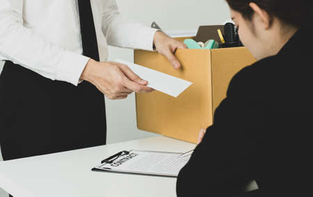 Desperately fired man office worker employee hands her employer her resignation letter and packs her...