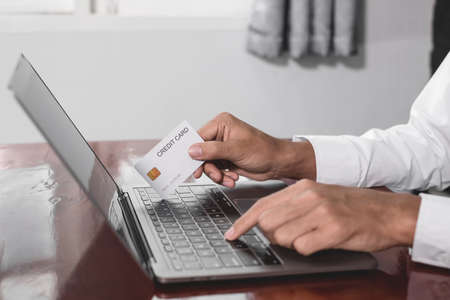 The businessman's hand is holding a credit card and using a laptop for online shopping and internet...