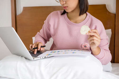 work from home, a young Asian woman who works in finance at home calculates financial graphs showing the results of his investments, planning the steps of his business growth.の写真素材