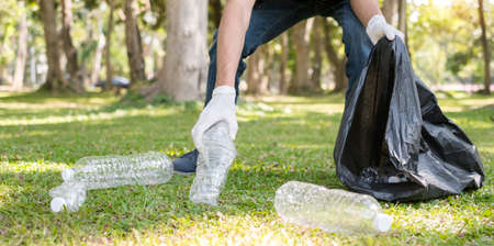 garbage collection, Man's hands pick up plastic bottles, put garbage in black garbage bags to clean up at parks, avoid pollution, be friendly to the environment and ecosystem.の写真素材