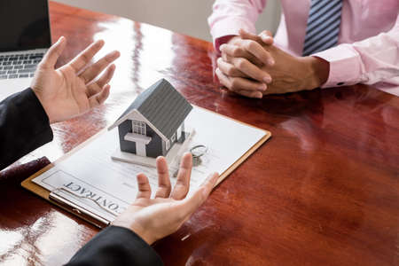 A real estate agent with a home model is talking to clients about renting a home and buying home...