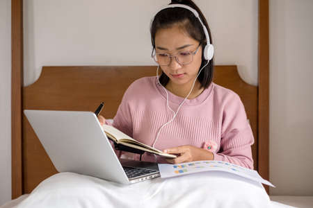 work from home, a young Asian woman who works in finance at home calculates financial graphs showing...