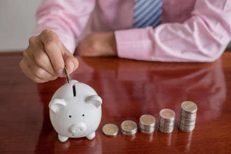 The hand of a businessman puts coins in a piggy bank, saves money with coins, steps into a successful growth business, and saves for retirement concept.の写真素材
