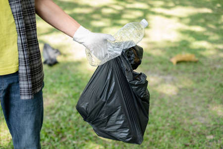 Garbage collection, Man's hands pick up plastic bottles, put garbage in black garbage bags to clean up at parks, avoid pollution, be friendly to the environment and ecosystem.の写真素材