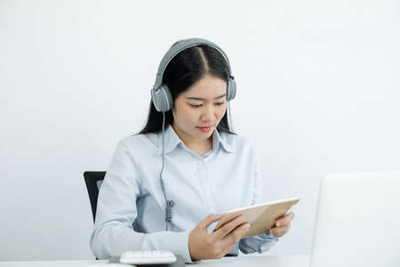Video call, a young Asian woman wearing headphones, communicates via online video long distance, looking at the digital laptop screen, happily greeted with a friend.の写真素材
