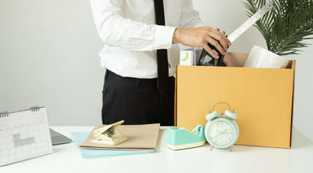A male office worker is unhappy with being fired from a company packing things into cardboard boxes. The young man was stressed and disappointed by being fired. concept of layoffs and unemployment.の写真素材