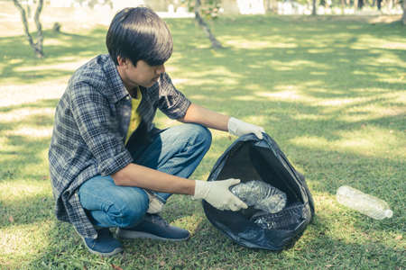 young Asian men, garbage collection pick up plastic bottles, put garbage in black garbage bags to clean up at parks, avoid pollution, be friendly to the environment and ecosystem.の写真素材