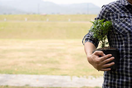 The young man's hands are planting young seedlings on fertile ground, taking care of growing plants. World environment day concept, protecting nature.の写真素材