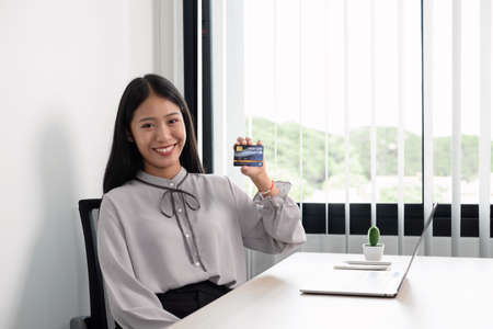 The Asian businesswoman's hand is holding a credit card and using a laptop for online shopping and...