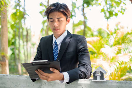 Home insurance concept and real estate. Business Asian man with house model working in investment about renting a house, buying a house, and home insurance.の写真素材