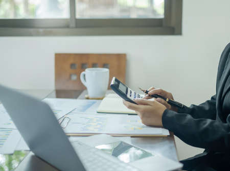 Asian female accountants sit at their desks and calculate financial graphs showing results about their investments, planning a successful business growth process.の写真素材