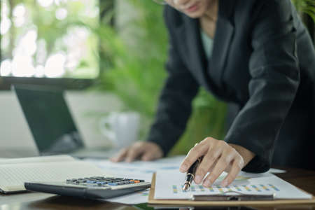Asian female accountants sit at their desks and calculate financial graphs showing results about their investments, planning a successful business growth process.の写真素材