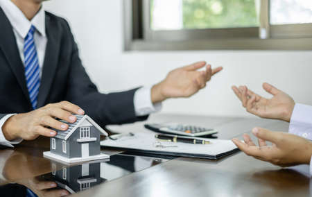 A real estate agent with a House model is talking to clients about buying home insurance. Home insurance concept.の写真素材