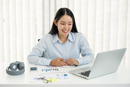 Asian woman working laptop. Successful smiling businesswoman sitting working and taking notes at the office.の写真素材