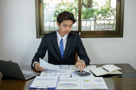 Young Asian businessman financial market analyst sits at their desks and calculate financial graphs showing the results of their investments planning the process of successful business growth.の写真素材