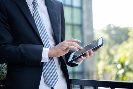 A picture of a businessman. Asian businessmen stand looking laptop in front of modern office buildings.の写真素材