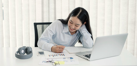 Asian woman working laptop. Successful smiling businesswoman sitting working and taking notes at the office.の写真素材
