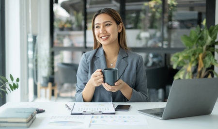 Asian businesswoman smiling happily with a new morning holding a cup of coffee lightly sipping coffee professional woman in size working in the office.の写真素材
