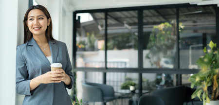 Asian businesswoman smiling happily with a new morning holding a cup of coffee lightly sipping coffee professional woman in size working in the office.の写真素材