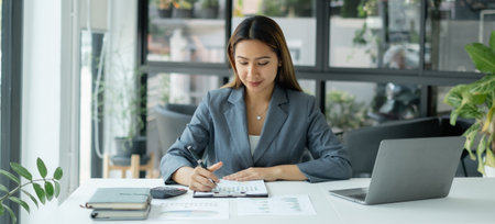 Asian businesswoman sit at their desks and calculate financial graphs showing results about their investments, plan a successful business growth process.の写真素材