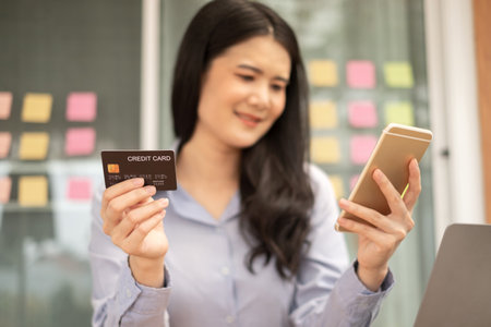 Asian girl shopping online holding credit and using smartphone enter their card number in the mobile phone app to purchase and payment in internet store.の写真素材
