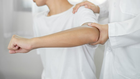 Female physiotherapists provide assistance to male patients with elbow injuries and examine patients in rehabilitation centers. Physiotherapy concepts.の写真素材