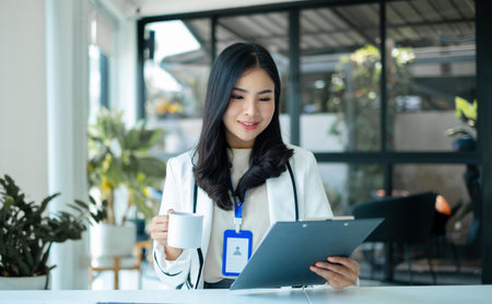 Asian businesswoman smiling happily with a new morning holding a cup of coffee lightly sipping coffee professional woman in size working in the office.の写真素材
