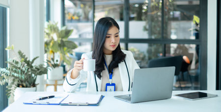 Asian businesswoman smiling happily with a new morning holding a cup of coffee lightly sipping coffee professional woman in size working in the office.の写真素材