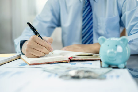 Man calculating her expenses on a notebook putting coin into piggy bank. Saving money with coins Step into a business that is growing to be successful and save for retirement concepts.の写真素材
