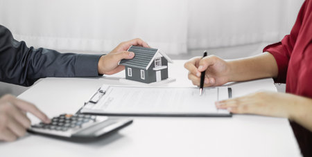 A real estate agent with a home model is talking to clients about renting a house and buying home insurance and contracting the contract after the formal negotiation is completed.の写真素材