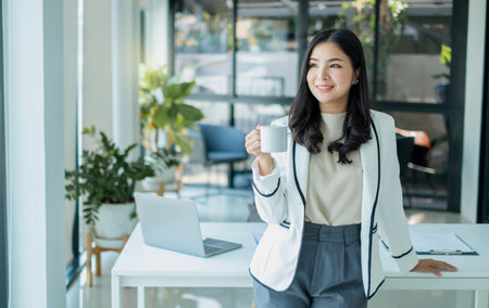 Asian businesswoman smiling happily with a new morning holding a cup of coffee lightly sipping coffee professional woman in size working in the office.の写真素材