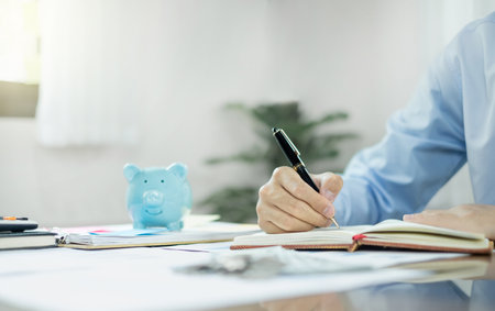 Man calculating her expenses on a notebook putting coin into piggy bank. Saving money with coins Step into a business that is growing to be successful and save for retirement concepts.の写真素材