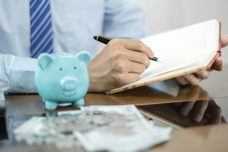 Man calculating her expenses on a notebook putting coin into piggy bank. Saving money with coins Step into a business that is growing to be successful and save for retirement concepts.の写真素材