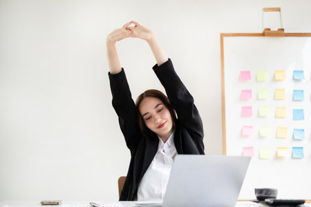 Asian female accountant is tired from working in a chair, stretching to relax and relax while working hard at the office.の写真素材
