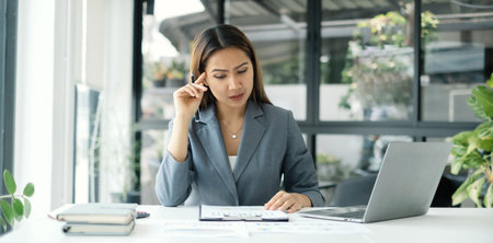Asian businesswomen sit at their desks and calculate financial graphs showing results about their investments, planning successful business growth process.の写真素材