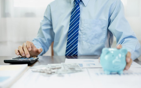 Man calculating her expenses on a notebook putting coin into piggy bank. Saving money with coins Step into a business that is growing to be successful and save for retirement concepts.の写真素材