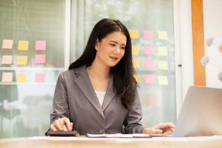 Asian businesswoman sit at their desks and calculate financial graphs showing results about their investments, plan a successful business growth process.の写真素材